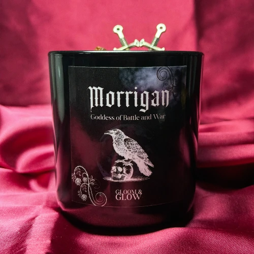 Ezoteryczna świeca rytualna Morrigan marki Gloom&amp;Glow w czarnym szkle z grafiką kruka, ustawiona na czerwonym, satynowym tle do rytuałów ochrony.