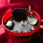 Zbliżenie na czarny wosk świecy ochronnej Lilith z zatopionym surowym obsydianem, kwarcem dymnym, granatem, heliotropem oraz srebrnym charmsem wężem.