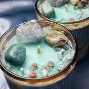 Dwie ezoteryczne świece sojowe dla znaku zodiaku Wodnik od gloomandglow. Kadr skupia się na bogatym wnętrzu pierwszej świecy, ukazując zatopione w wosku surowe kamienie szlachetne i talizmany.
