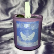 Fioletowa ezoteryczna świeca sojowa Hypnos marki Gloomandglow z etykietą ze skrzydłami i kryształami na satynowym tle.