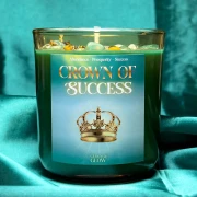 Zielona świeca intencyjna Crown of Success w szklanym słoiku na tle eleganckiego, szmaragdowego materiału.