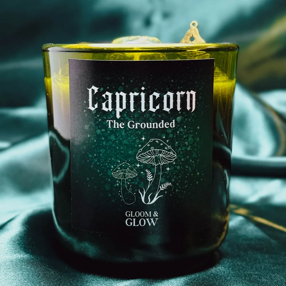 Ciemnozielona świeca sojowa dla znaku zodiaku Koziorożec marki Gloomy Glow, ustawiona na tle błyszczącej, szmaragdowej satyny..webp