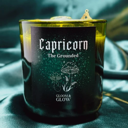 Ciemnozielona świeca sojowa dla znaku zodiaku Koziorożec marki Gloomy Glow, ustawiona na tle błyszczącej, szmaragdowej satyny..webp