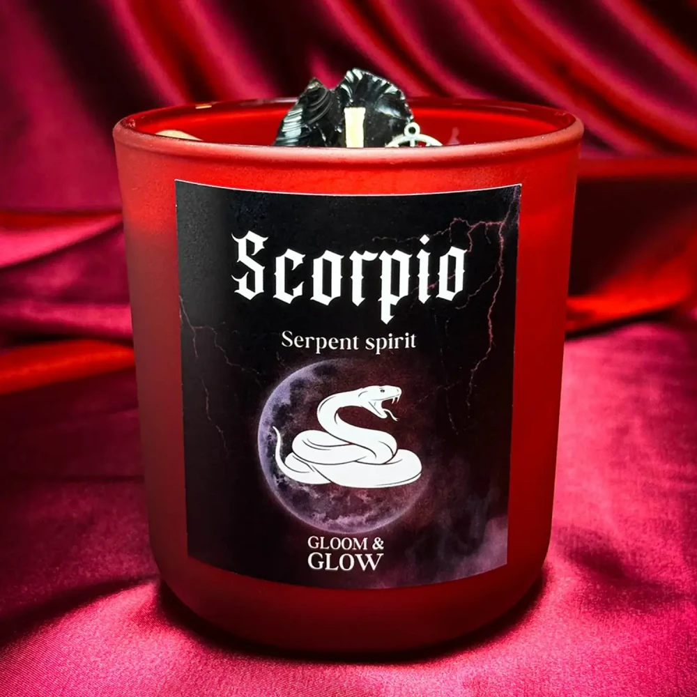 Czerwona świeca sojowa dla znaku zodiaku Skorpion z grafiką węża i napisem Serpent Spirit, ustawiona na błyszczącej czerwonej satynie
