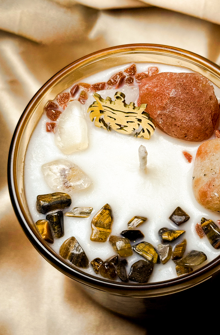Zbliżenie na powierzchnię ręcznie robionej ezoterycznej świecy sojowej z zatopionymi naturalnymi kryształami, minerałami i złotym amuletem tygrysa.