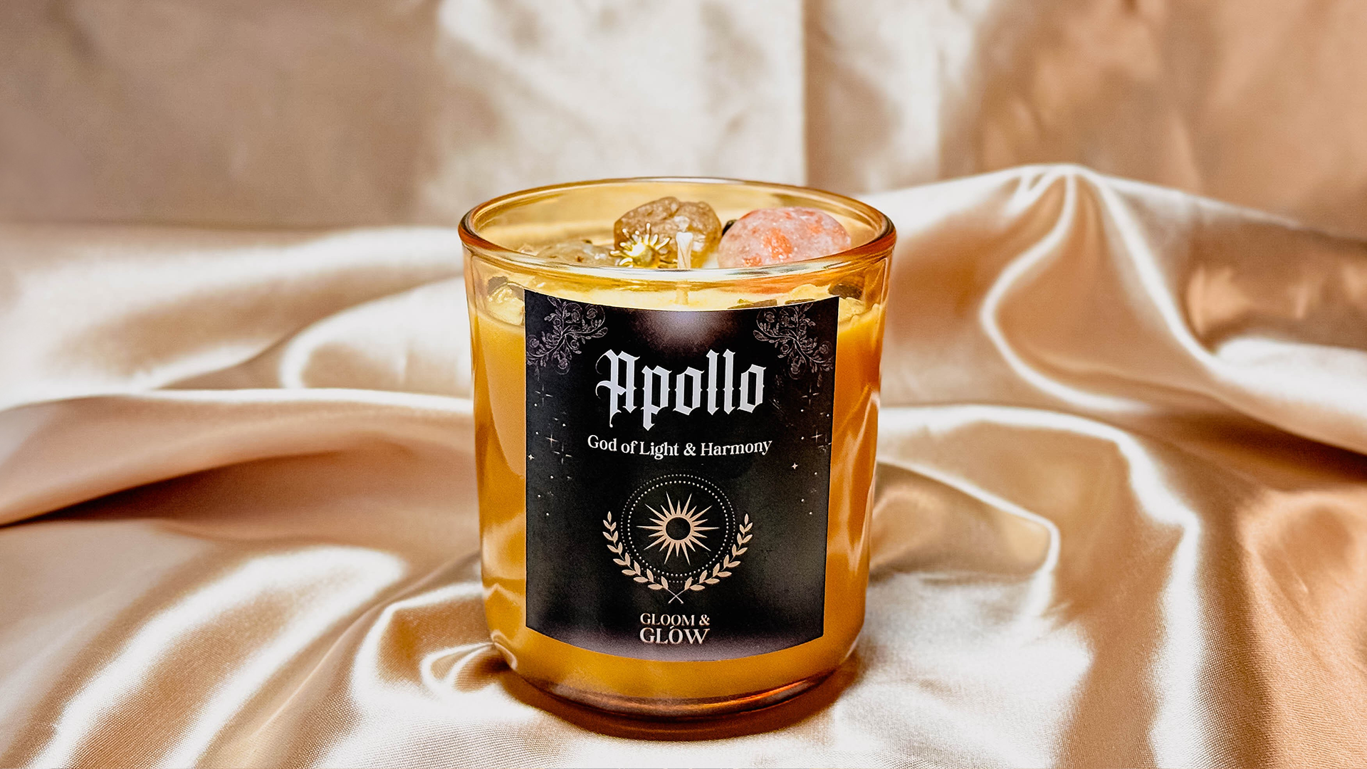 Złota świeca intencyjna Apollo od Gloom & Glow z kryształami na tle satynowego materiału – magia archetypów